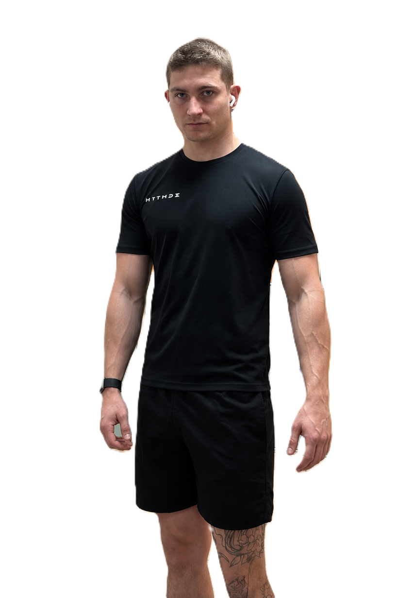 A man modeling a black short-sleeve athletic t-shirt and matching black shorts against a solid white background.