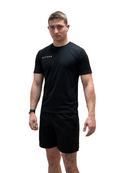 A man modeling a black short-sleeve athletic t-shirt and matching black shorts against a solid white background.