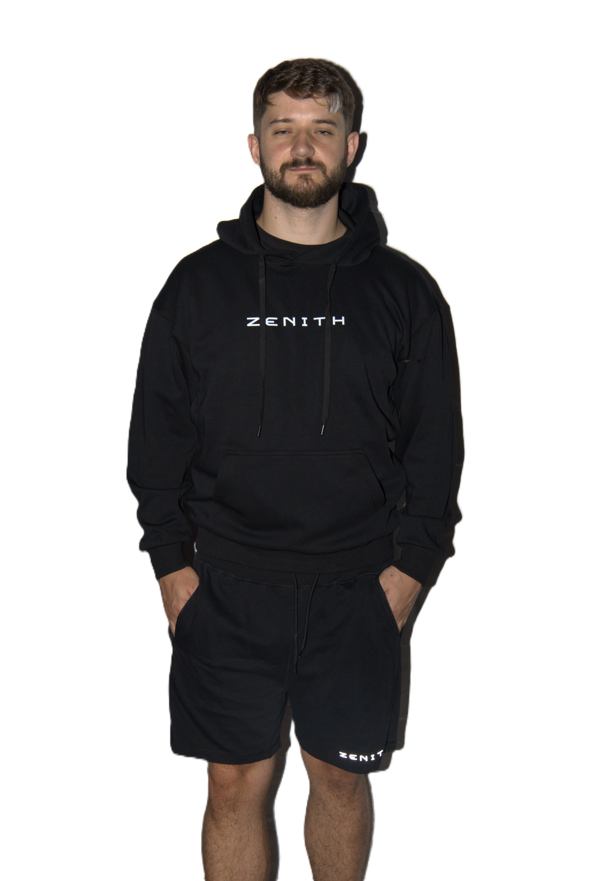 A man wearing a black Zenith hoodie and matching black shorts with white logo text, standing against a solid white background.