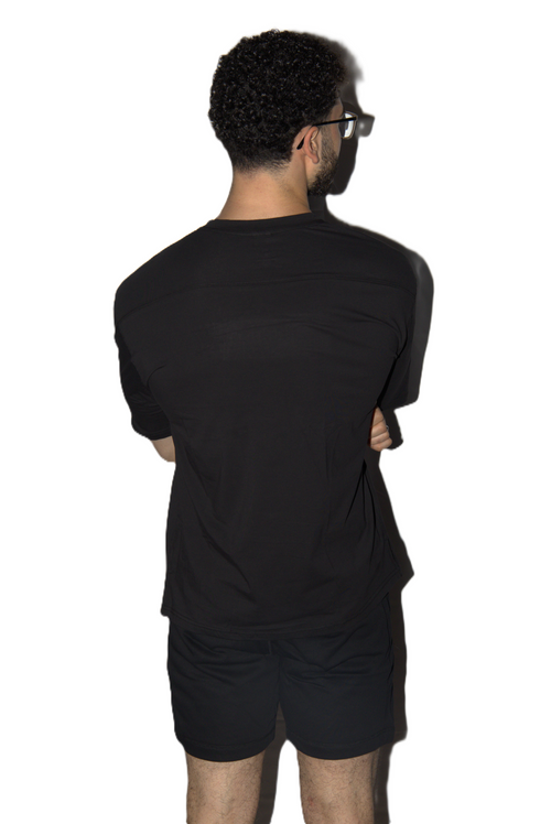 A man viewed from behind wearing a black short-sleeve t-shirt and matching black shorts against a plain white background.